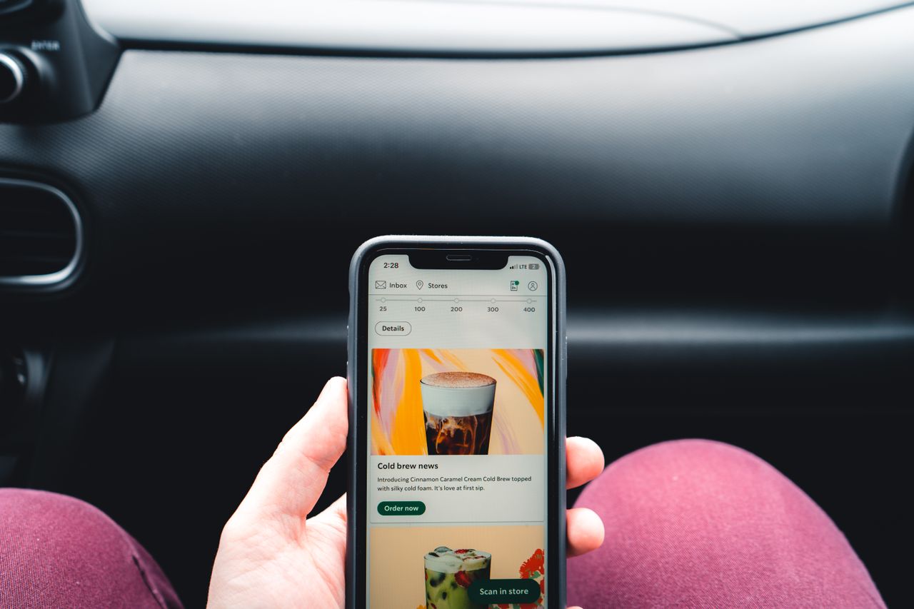 Crafting Captivating Headlines: Your awesome post title goes here Close-up of hand holding smartphone displaying coffee app menu inside car.