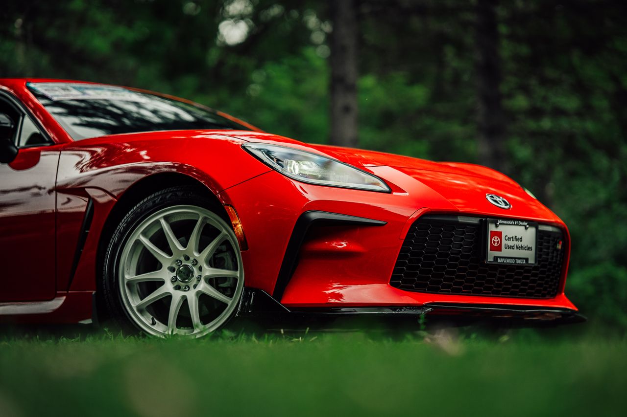 our-story-01 Red sports car showcased with vibrant color and sleek design in a natural outdoor environment.